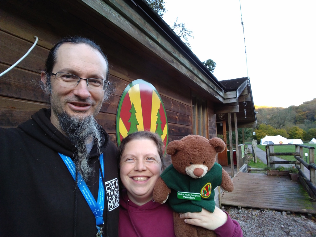 Couple wearing woodcraft hoddies and wardens's badges stading outside the cabin